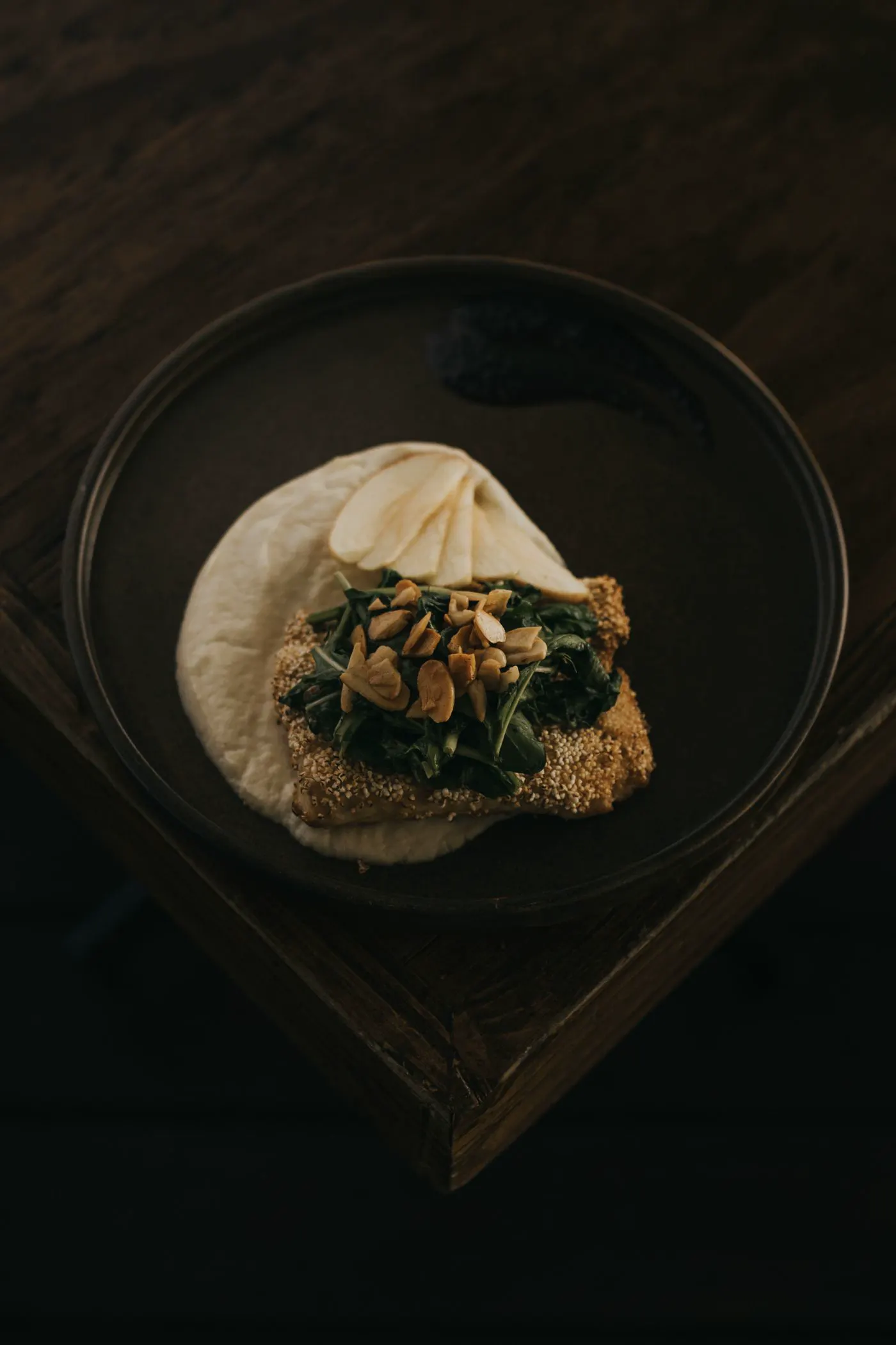 Greens and nuts over a creamy base on a dark plate.