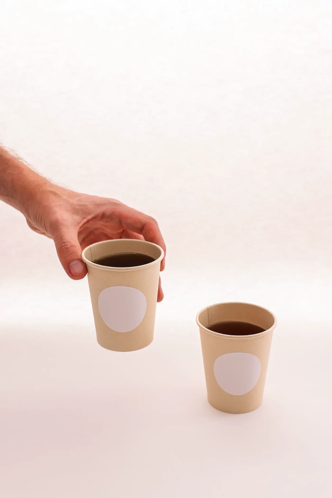 A hand picks up one of two plain kraft takeaway coffee cups.