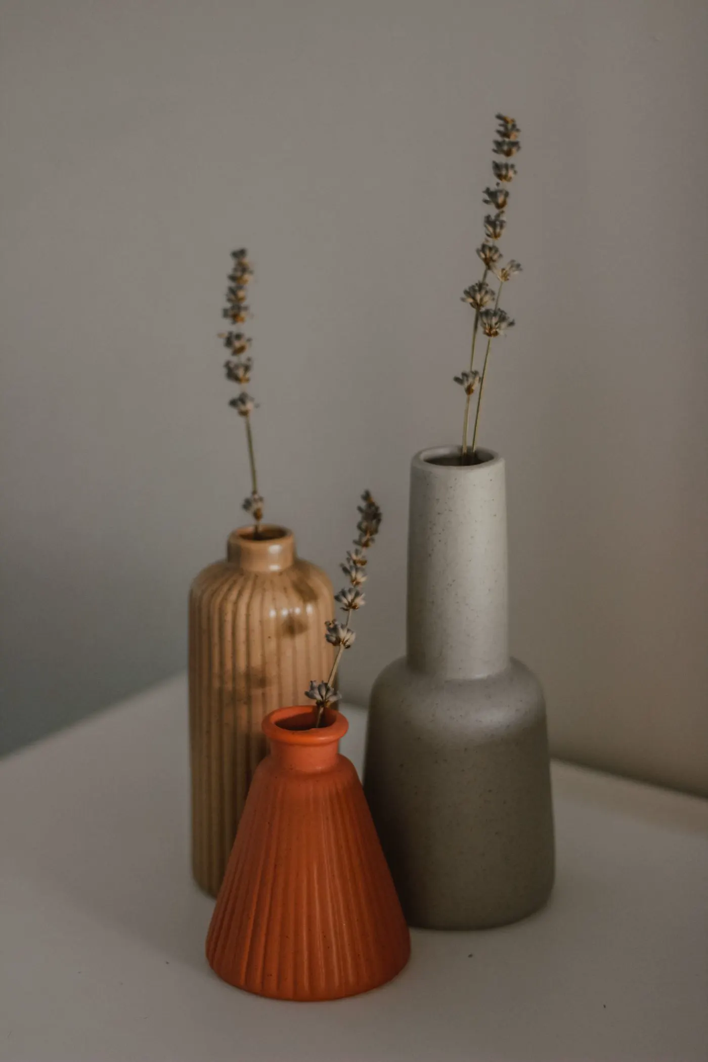 Terracotta and stone vases with dried stems on a pale table.