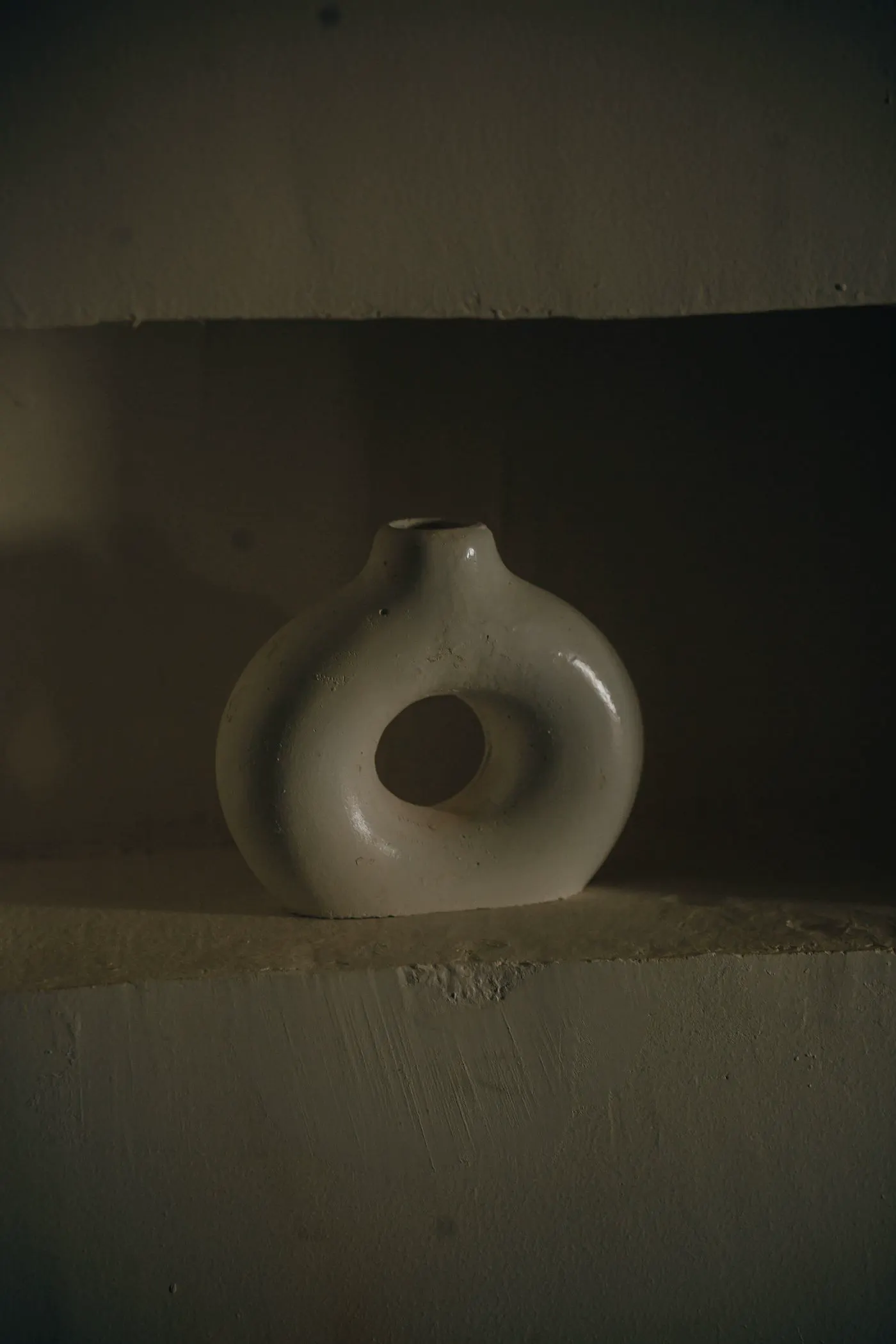 A round open ceramic vase on a dark shelf.