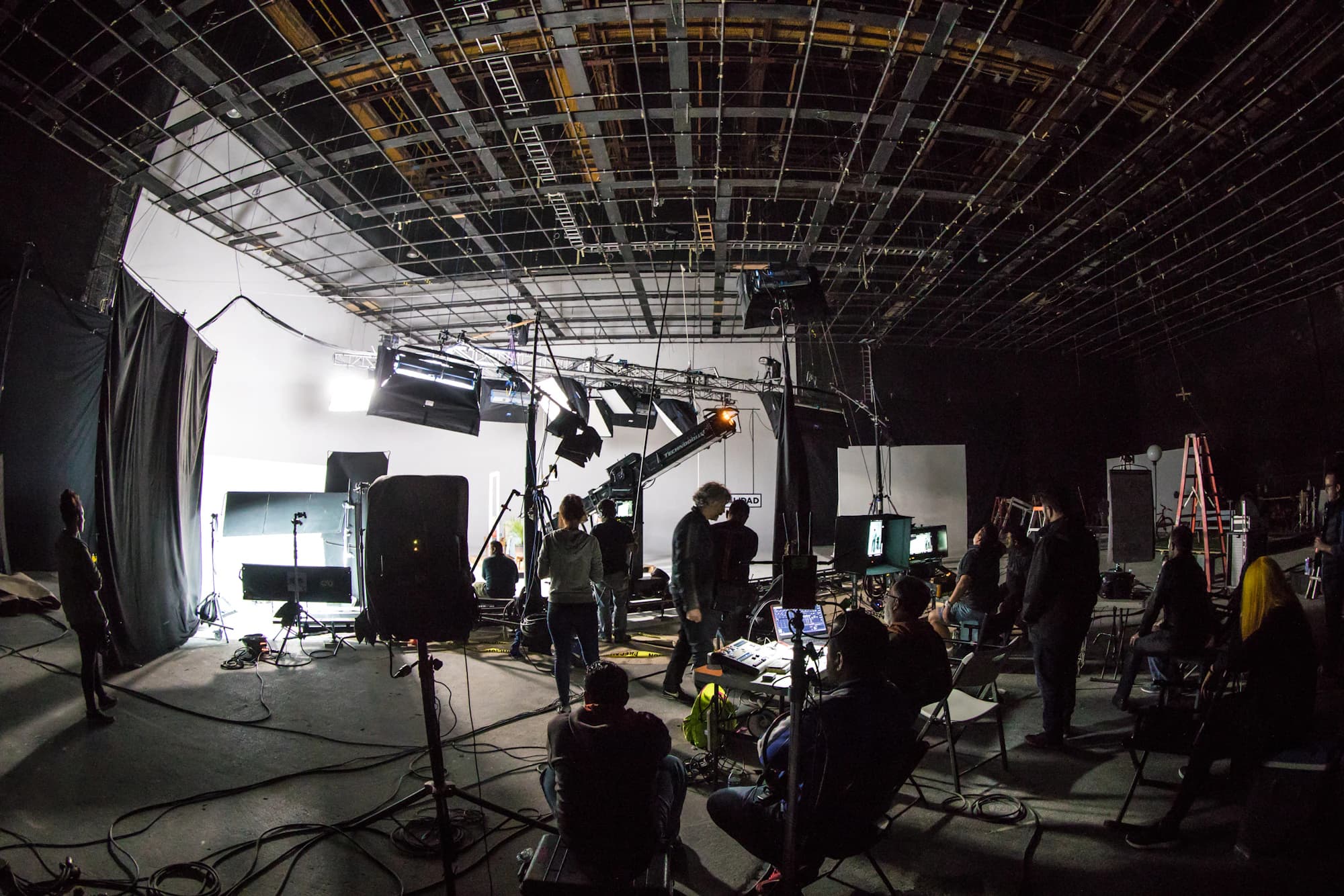 A film crew working on a large soundstage with lighting rigs and cameras.